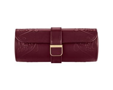 WOLF X LIBERTY Ianthe Triple Watch Roll shown from a straight front view, showcasing a sleek cylindrical silhouette in deep burgundy, featuring a selectively debossed art nouveau floral pattern on the sides and a centered leather snap-closure strap with a