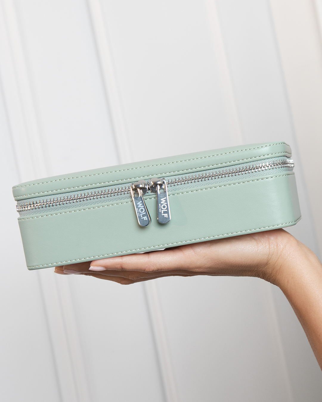 WOLF x Liberty Medium Jewellery Zip Case. WOLF x Liberty Medium Jewelry Zip Case in green, shown resting on a hand with gold-finish zip pulls.
